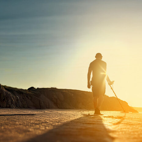 Nokta Legend 2 SMF Metal Detector Beach Detecting at Sunset Person using a Nokta Legend 2 SMF metal detector on a sandy beach at sunset with rocky cliffs.