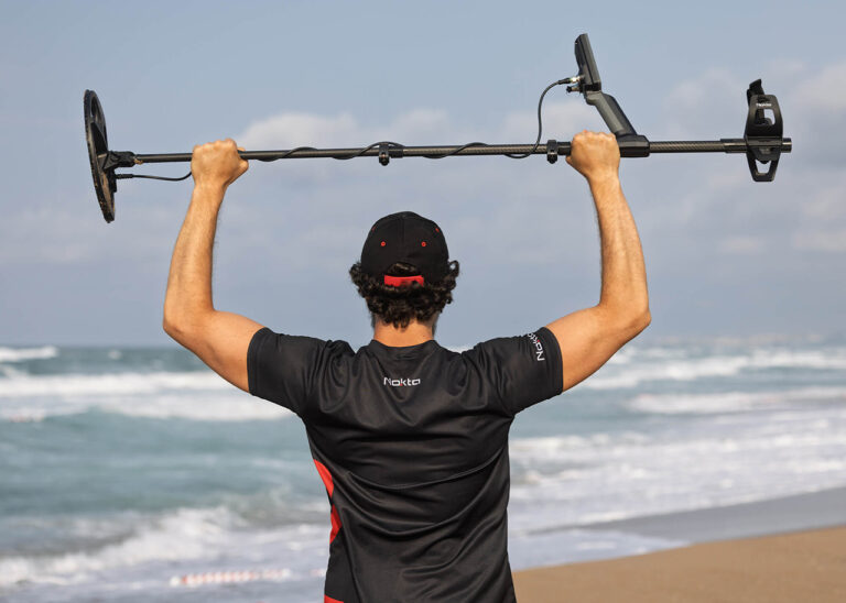 Nokta Legend 2 SMF Metal Detector Beach Performance Nokta Legend 2 SMF metal detector held high by a man on a beach, featuring a carbon fiber shaft and search coil.